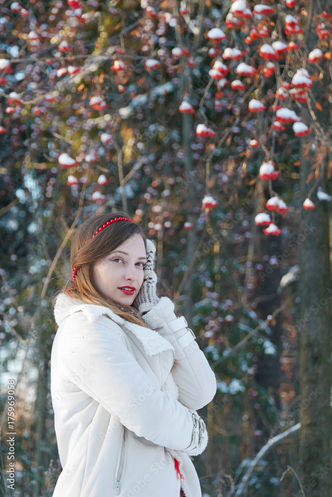 beautiful girl in a white dress is standing sideways, smiling looking at camera on background of a winter forest. she is happy and calm. beautiful girl in a white dress is standing sideways, smiling looking at camera on background of a winter forest. she is happy and calm.
