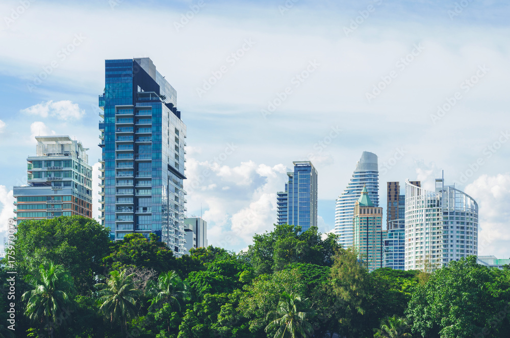 cityscape of high rise building or skyscraper with green tree in park against blue sky and cloud.