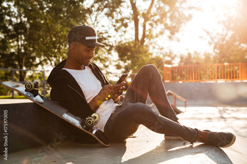 Photography Young african man with a skateboard using smartphone