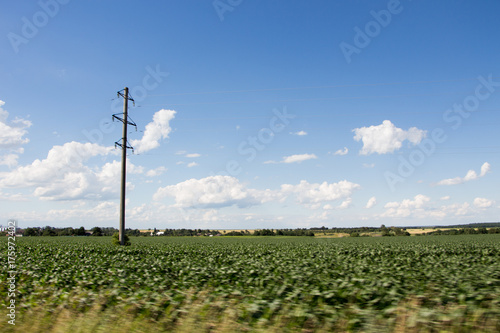 Picture at hight speed. Electric pole, green field and blue cloudy sky. 