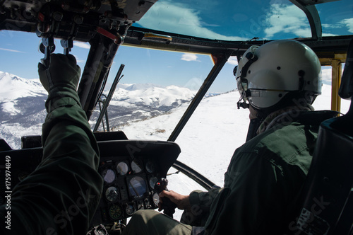 Pilot flying a military helicopter at the Andes Mountains during winter, cockpit view