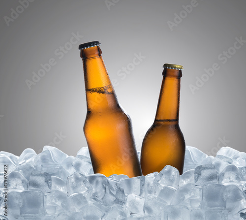 Cold bottle of beer with drops in ice cubes over gray background