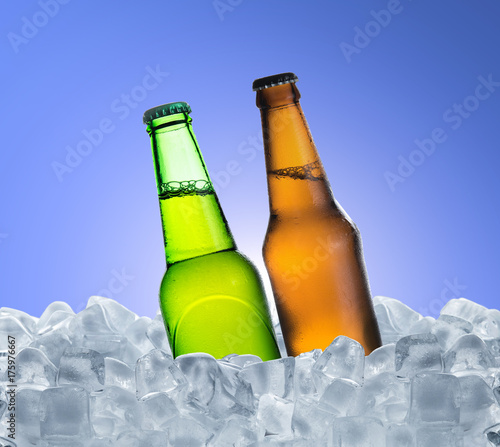 Cold bottle of beer with drops in ice cubes over blue background