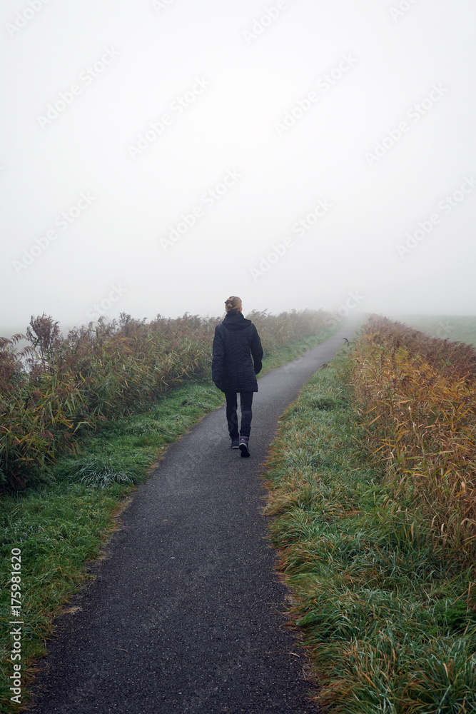 Woman walking on path on foggy day in autumn Woman walking on path on foggy day in autumn