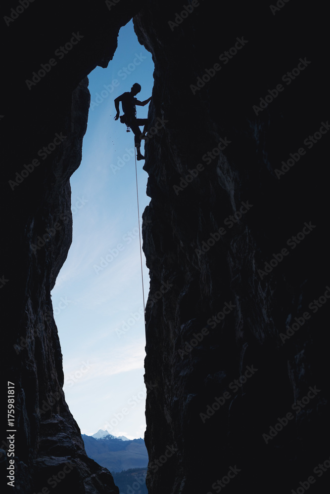 Alpinist silhouette climbing a rock cave entrance outdoor Alpinist silhouette climbing a rock cave entrance outdoor