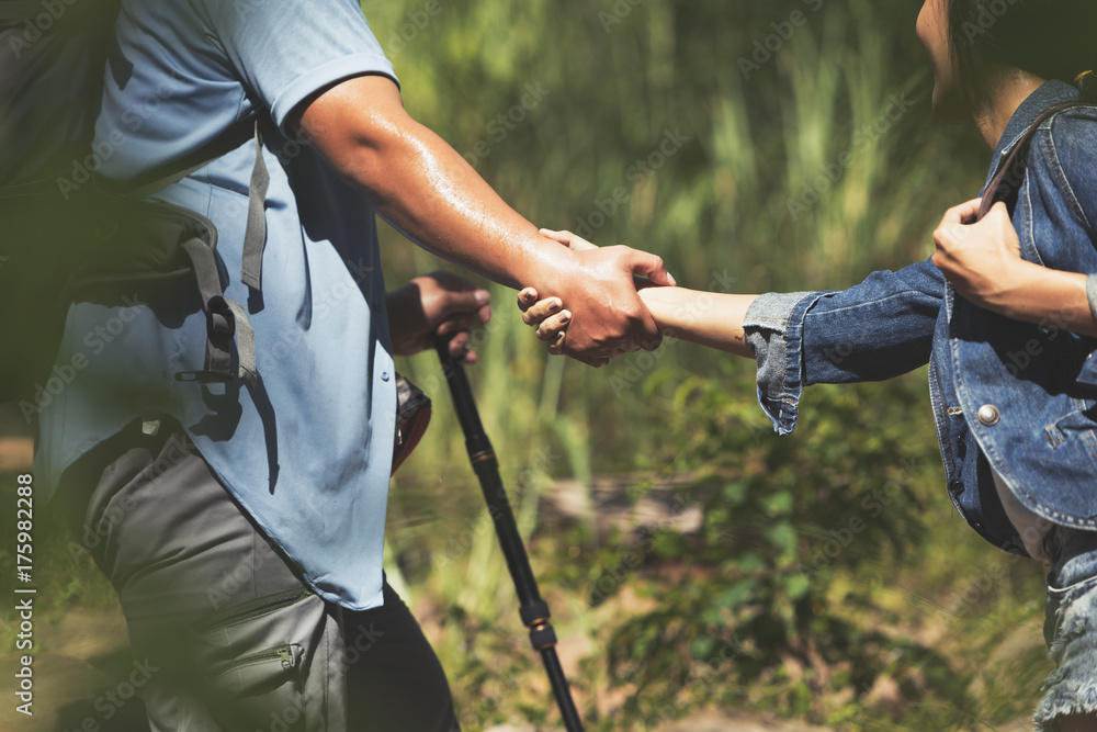 Obraz premium The hiking man is pulling his lover hand to help prevent falling while hiking.