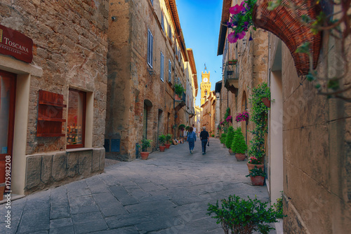 Beautiful narrow street with sunlight and flowers in the small magical and old village of Pienza  Val D Orcia Tuscany  Italy.