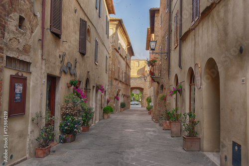 Beautiful narrow street with sunlight and flowers in the small magical and old village of Pienza  Val D Orcia Tuscany  Italy.