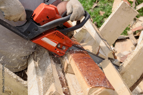 man saws wood with orange chainsaw