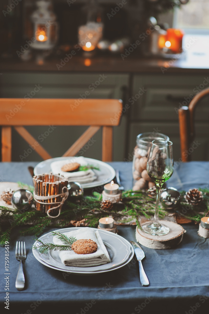 Festive Christmas and New Year table setting in scandinavian style with rustic handmade details in natural and white tones. Dining place decorated with pine cones, branches and candles