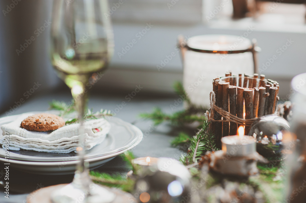 Festive Christmas and New Year table setting in scandinavian style with rustic handmade details in natural and white tones. Dining place decorated with pine cones, branches and candles Festive Christmas and New Year table setting in scandinavian style with rustic handmade details in natural and white tones. Dining place decorated with pine cones, branches and candles