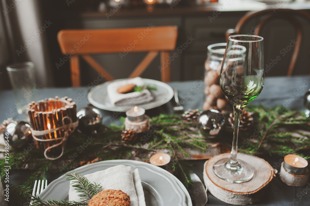 Fototapeta premium Festive Christmas and New Year table setting in scandinavian style with rustic handmade details in natural and white tones. Dining place decorated with pine cones, branches and candles