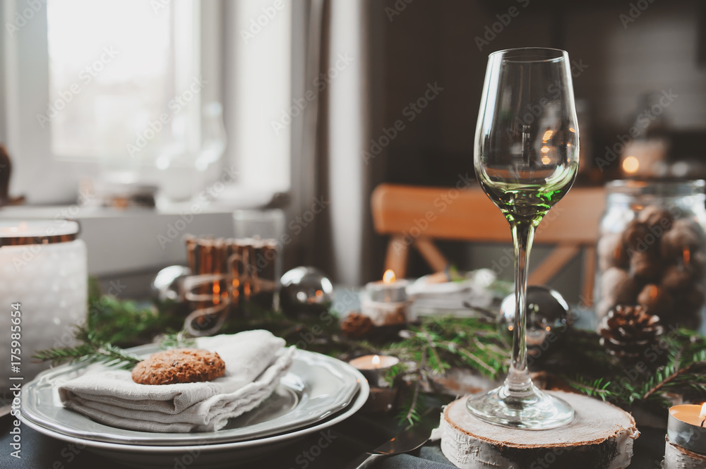 Festive Christmas and New Year table setting in scandinavian style with rustic handmade details in natural and white tones. Dining place decorated with pine cones, branches and candles