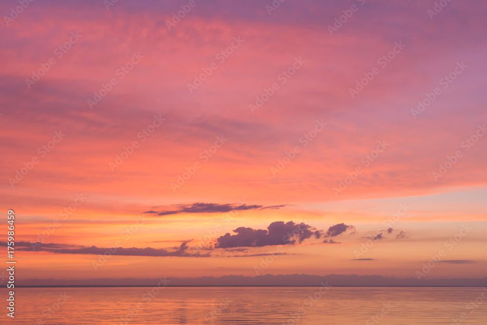 Serene tender pink sunset on the ocean with small clouds. Background for calmness