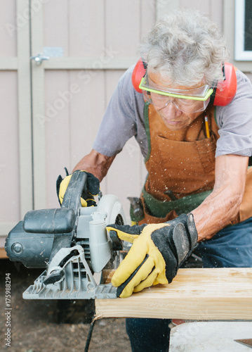 Elderly woman carpenter using circular hand saw to cut lumber