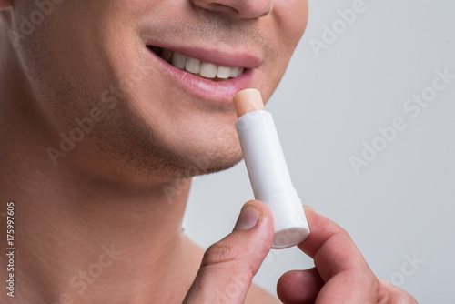 Cheerful naked man is using cosmetic balm