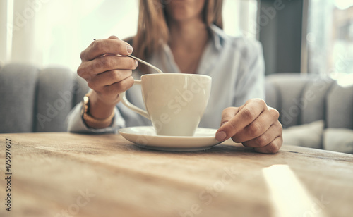 A girl is sitting in a cafe. Drinking tea. Coffee. White cup with coffee. Stir sugar. Holds a cup of coffee in his hand. Pastel shades. Close-up