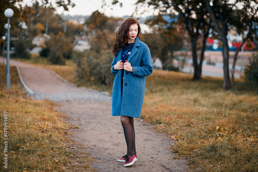 Fashionable young curly woman in autumn in park smiling wearing blue coat and red sneakers Fashionable young curly woman in autumn in park smiling wearing blue coat and red sneakers