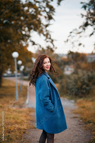 Fashionable young curly woman in autumn in park smiling and turning wearing blue coat