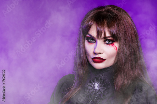 Witch  a vampire in a black gothic dress on a purple background. Portrait. American  dress for a costume party Halloween. Bright makeup