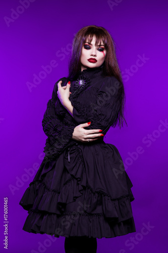 Witch, a vampire in a black gothic dress on a purple background. American, dress for a costume party Halloween. Bright makeup