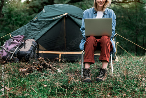 Cheerful young woman resting with gadget in forest