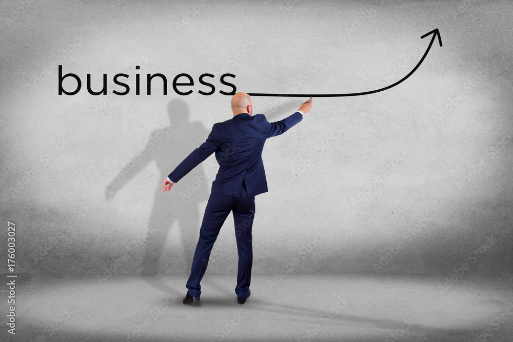 Obraz premium Businessman in front of a wall writing the word business with a arrow - business concept