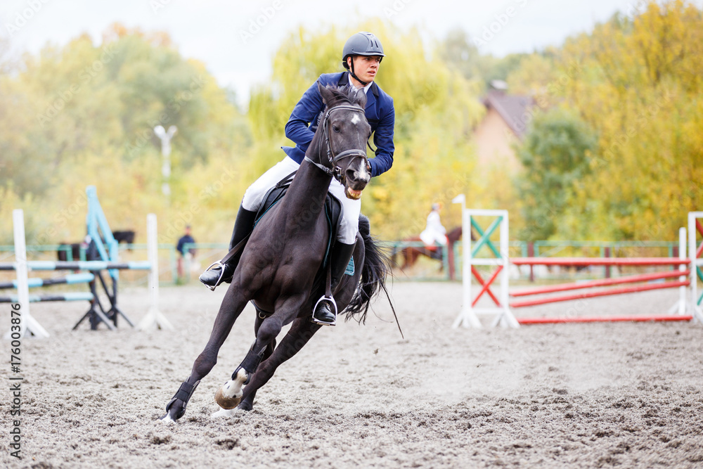 Young rider man on bay horse galloping on his course at show jumping competition Young rider man on bay horse galloping on his course at show jumping competition