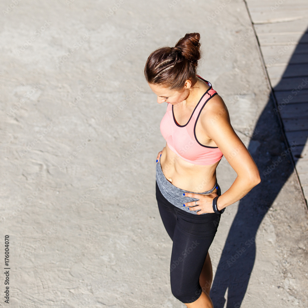 Young slim girl resting after run training in the park. Smiling runner woman standing outdoors