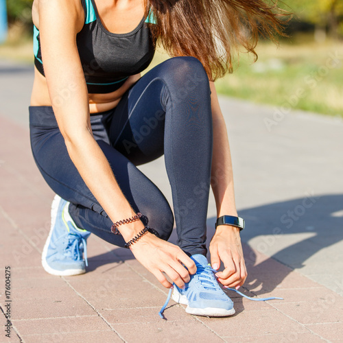 Young woman runner lacing up shoelaces on the trail jogging in park