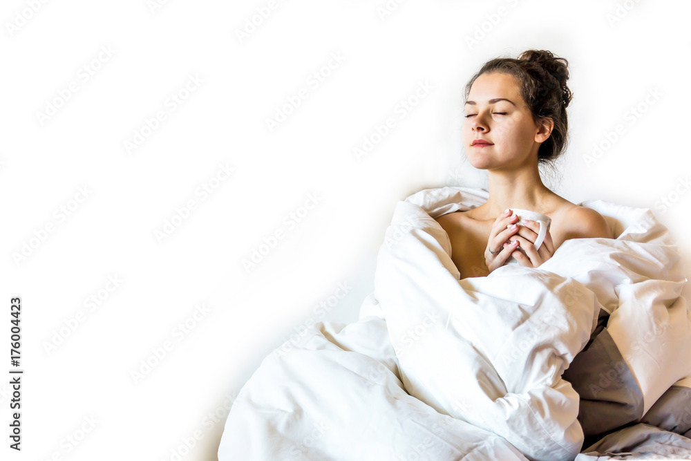 Beautiful young woman covered by blanket is sitting on bed with hot tea Beautiful young woman covered by blanket is sitting on bed with hot tea