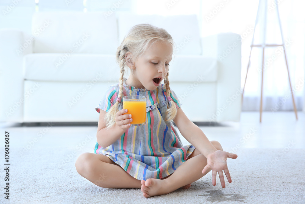 Cute little girl with glass of juice sitting on carpet near wet spot - obrazy, fototapety, plakaty 