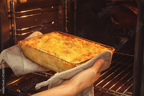 Woman taking baking tray with spinach lasagna out of oven photo