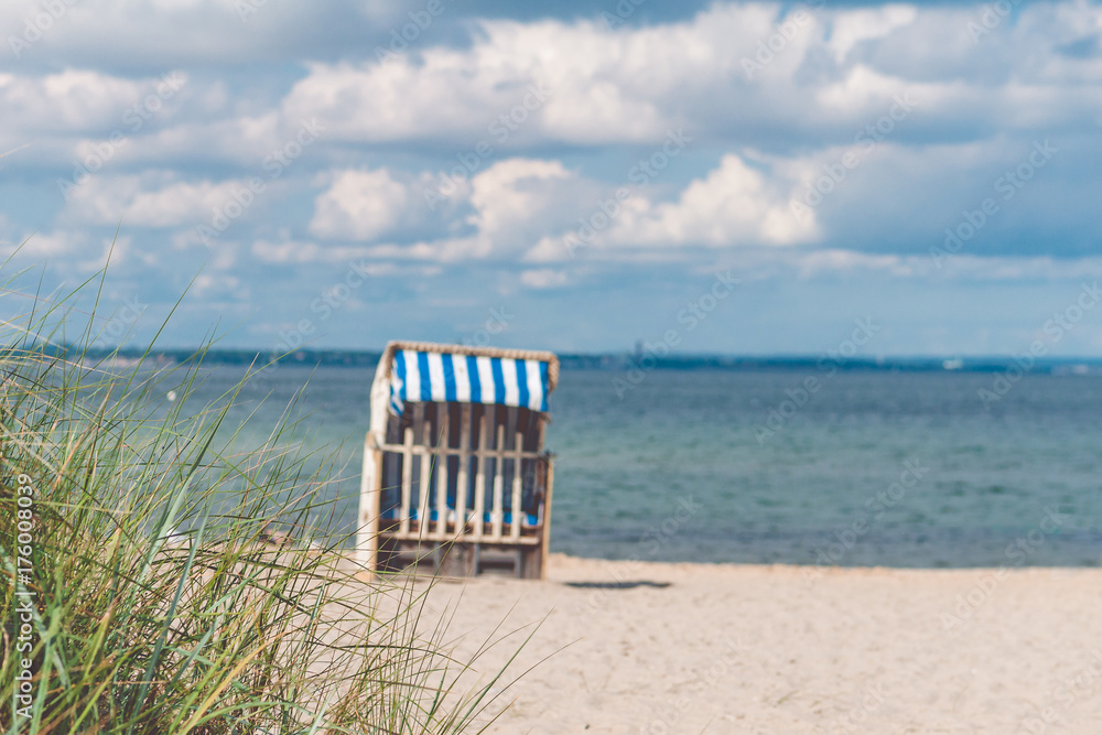 Blue colored roofed chairs on sandy beach in Travemunde. Grass bush in foreground. Germany