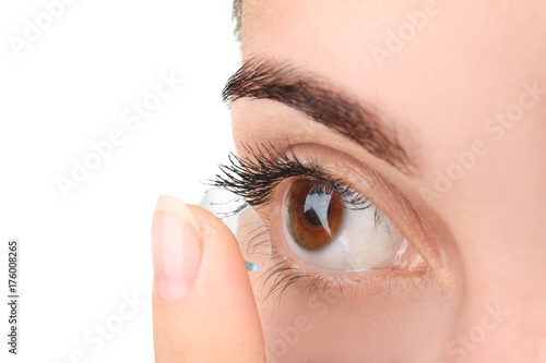 Fototapeta Naklejka Na Ścianę i Meble -  Young woman putting contact lens on light background, closeup