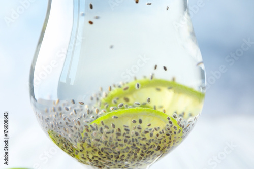 Glass of water with chia seeds and lime slices on light background, closeup
