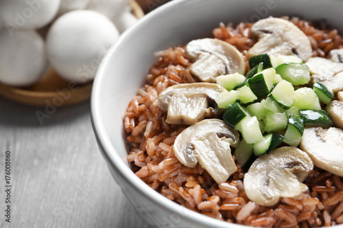 Bowl with tasty brown rice, zucchini and mushrooms on table, closeup