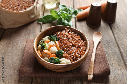 Bowl with tasty brown rice and vegetables on wooden table