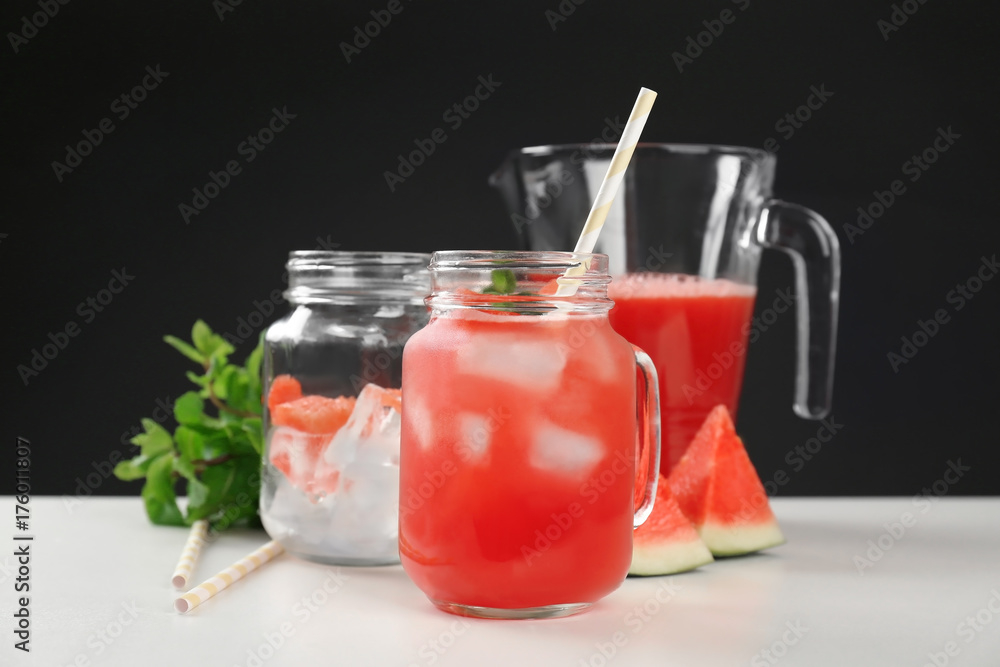 Jug and mason jars with watermelon juice on table against black background Jug and mason jars with watermelon juice on table against black background