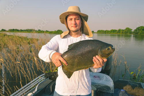 Man using hat and white shirt holding a fish on board of a boat