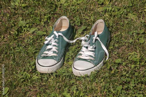 Old used weathered green sneakers closeup on grass background © varbenov