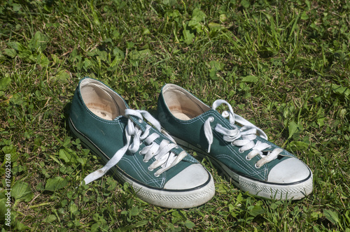 Old used weathered green sneakers closeup on grass background
