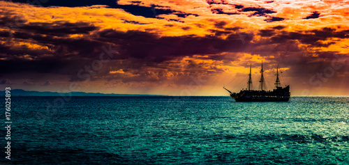 A lone ship against the morning sky. A distant historic ship in dramatic atmosphere.