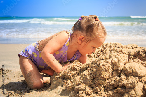 Little Blond Girl Squats Builds Sand Castle on Beach Closeup
