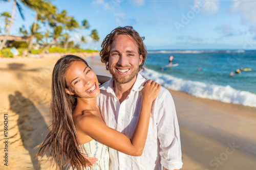 Couple in love hugging happy together on beach travel holidays at sunset. Beautiful Asian woman and caucasian man portrait. Young couple lovers relaxing on honeymoon. © Maridav