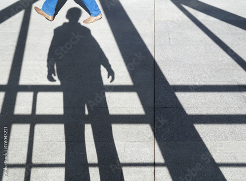 shadow of a man on the sidewalk among the beams, visible someone's feet