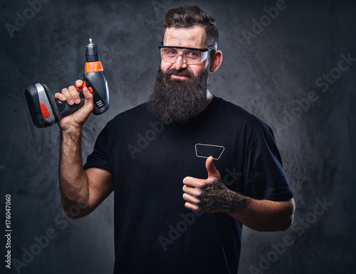 A man holds a drill over grey background.