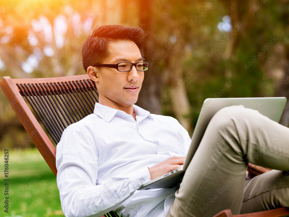 Fototapeta premium Young businessman using laptop while sitting outdoors
