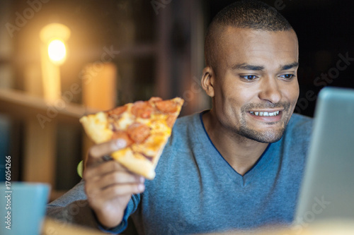 Positive delighted international man holding pizza