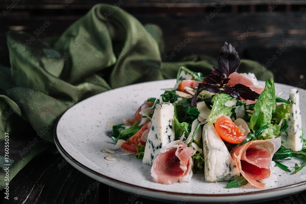 Green salad with prosciutto and blue cheese served with fabric on dark wooden background